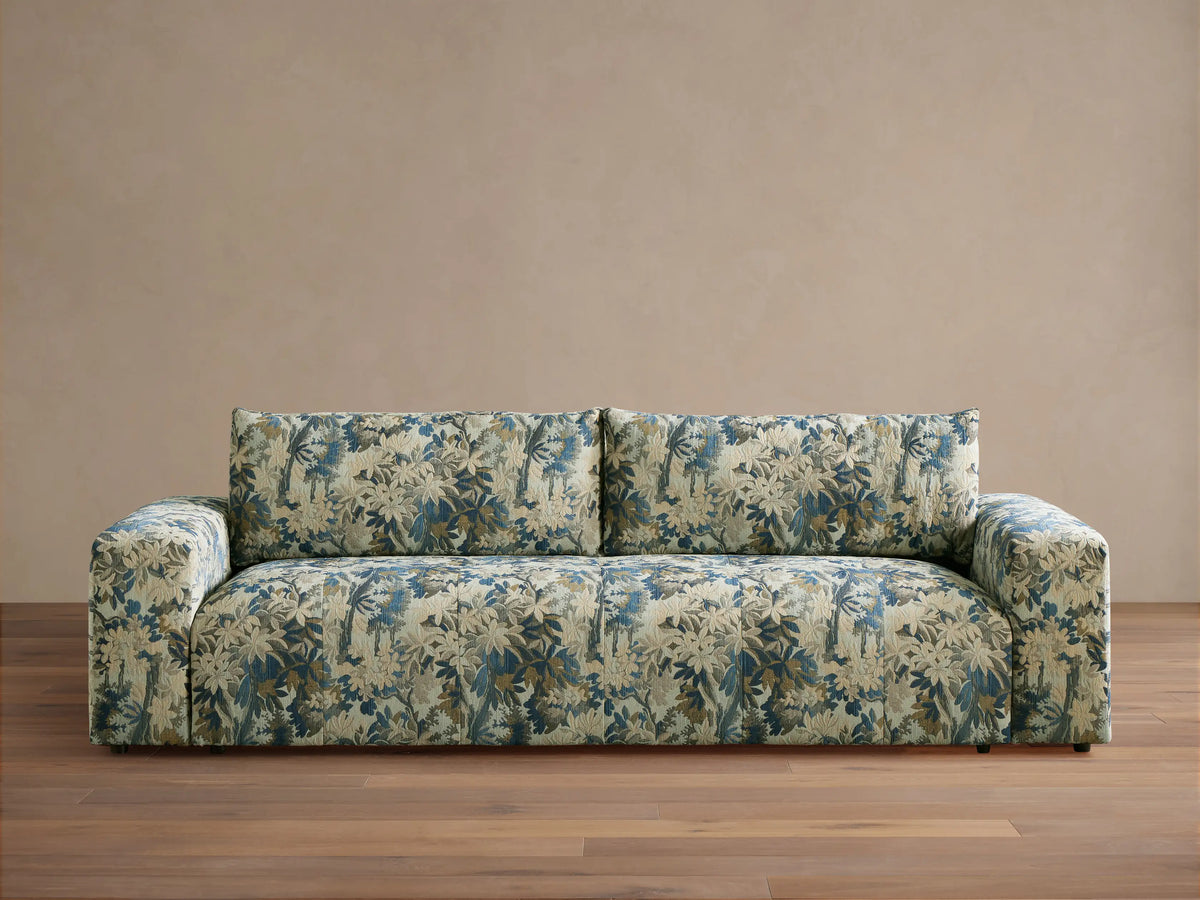 Keegan Sofa in a blue, cream, and brown botanical pattern, featuring wide arms and soft cushions, on a wooden floor.