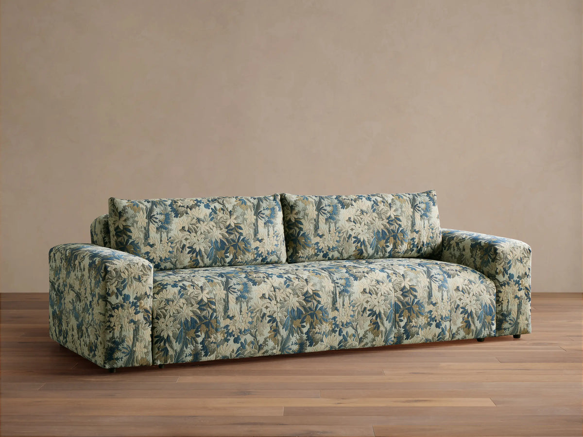 Keegan Sofa in a blue, cream, and brown botanical pattern, featuring wide arms and soft cushions, on a wooden floor.