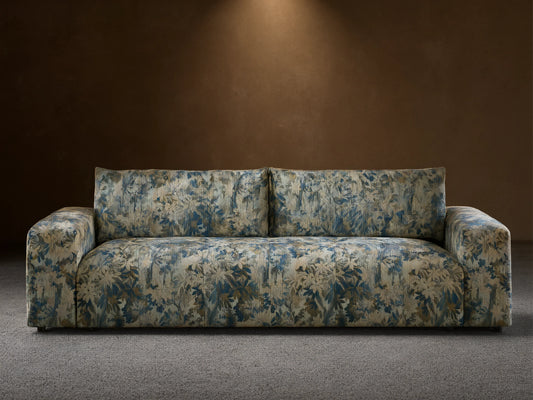 Keegan Sofa in a blue, cream, and brown botanical pattern, featuring wide arms and soft cushions, on a wooden floor.