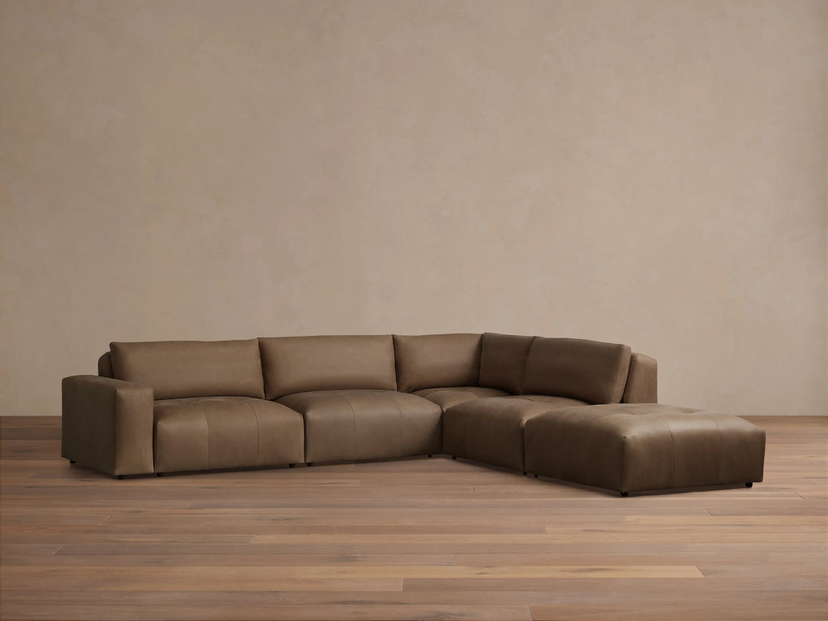 Keegan Leather Five-Piece Sectional in brown leather, arranged in an L-shape on wood flooring, against a beige wall.