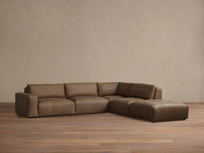 Keegan Leather Five-Piece Sectional in brown leather, arranged in an L-shape on wood flooring, against a beige wall.