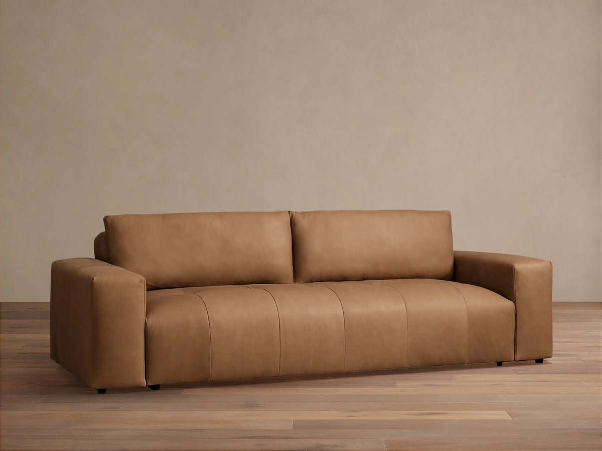 Keegan Leather Sofa, a modern, sleek tan leather sofa with block arms, centered against a light beige wall and wood floor.