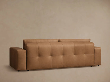 Close-up of a warm brown Keegan Leather Sofa, showing smooth, tufted seat cushions with stitching and a visible armrest.