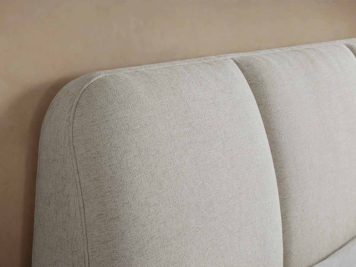 Kinnan Bed in beige fabric, side view. Features a tall, angled headboard with crisp white bedding tucked neatly, on dark wood legs.
