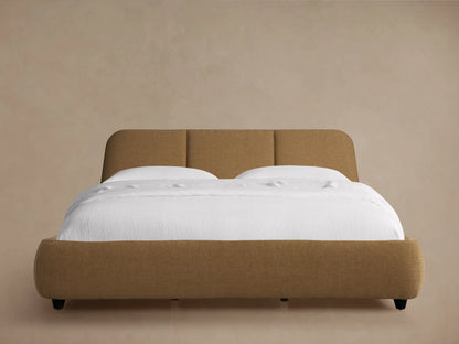 Kinnan Bed in tan fabric with a padded headboard, set against a neutral wall. White bedding is neatly arranged on the mattress.