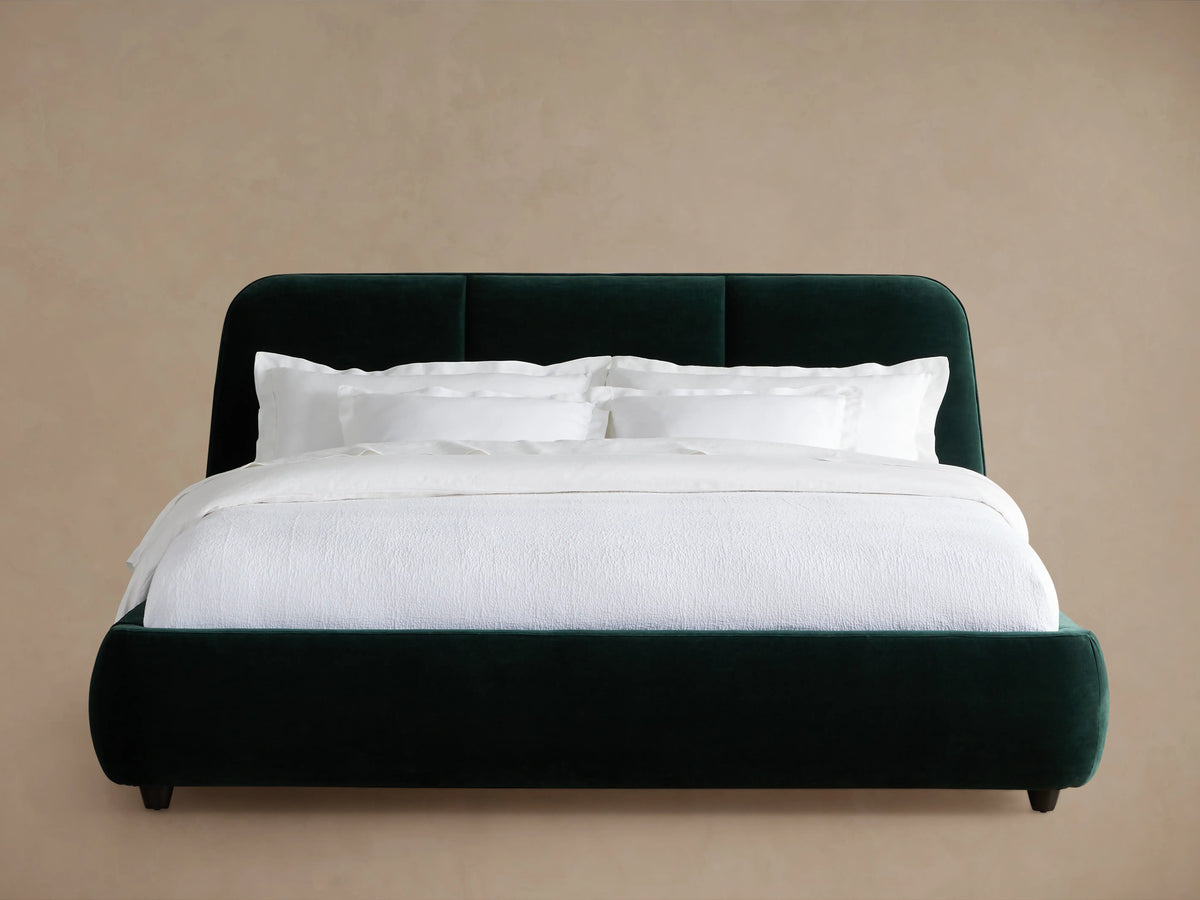 Kinnan Bed with dark green upholstered frame, rounded corners, and white bedding, against a beige background.