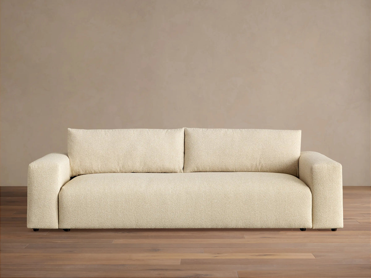 Keegan Tailored Sofa, light beige textured fabric. Modern style, two back cushions, wide square arms, on a wooden floor.