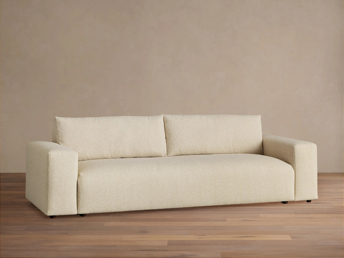 Keegan Tailored Sofa, light beige textured fabric. Modern style, two back cushions, wide square arms, on a wooden floor.