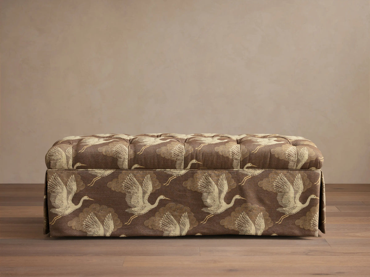 Front view of the brown Liddie Bench with a tufted top, skirted base, and light brown crane bird pattern.