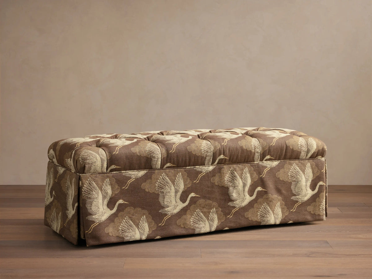 Front view of the brown Liddie Bench with a tufted top, skirted base, and light brown crane bird pattern.