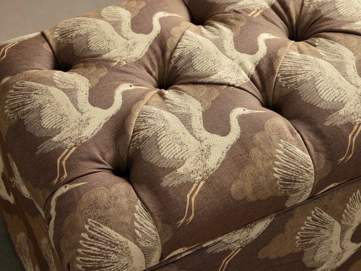 Front view of brown Liddie Bench with tufted top and pleated skirt featuring a beige flying crane and cloud pattern.