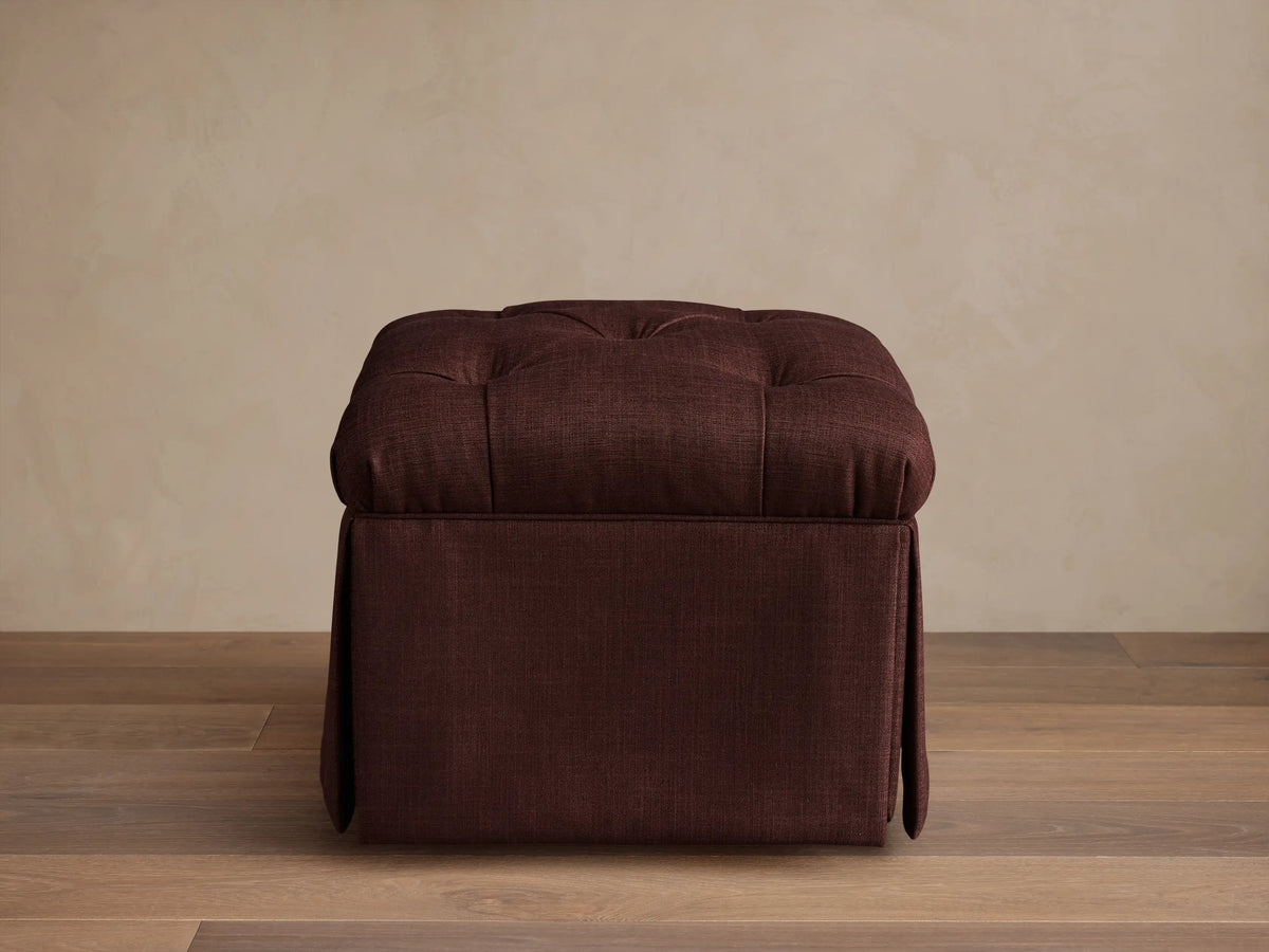 Front view of the burgundy Liddie Square Ottoman with a tufted top and pleated skirt.