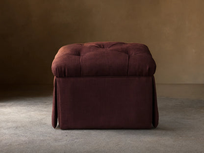 Front view of the burgundy Liddie Square Ottoman with a tufted top and pleated skirt.