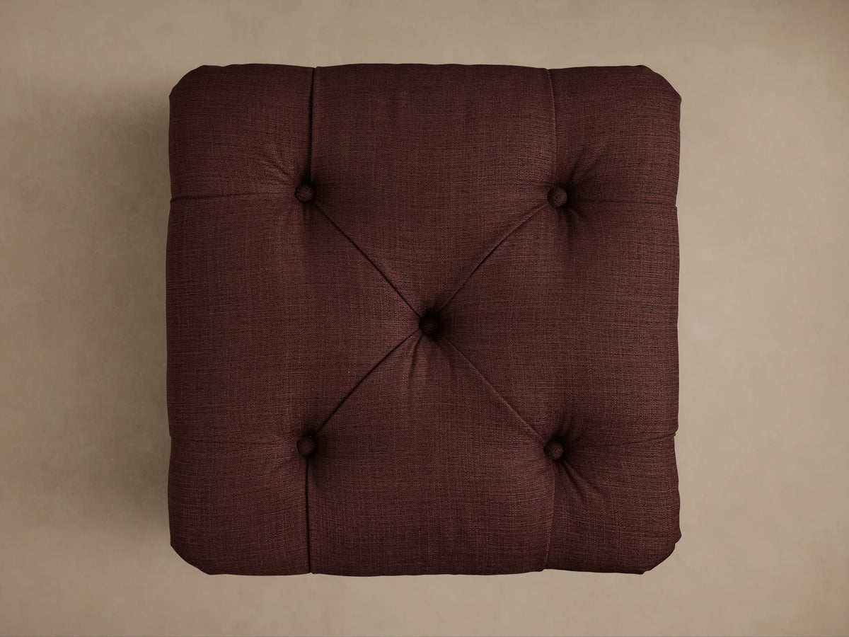 Burgundy Liddie Square Ottoman with a tufted top and a pleated skirted base, shown from an angled view.