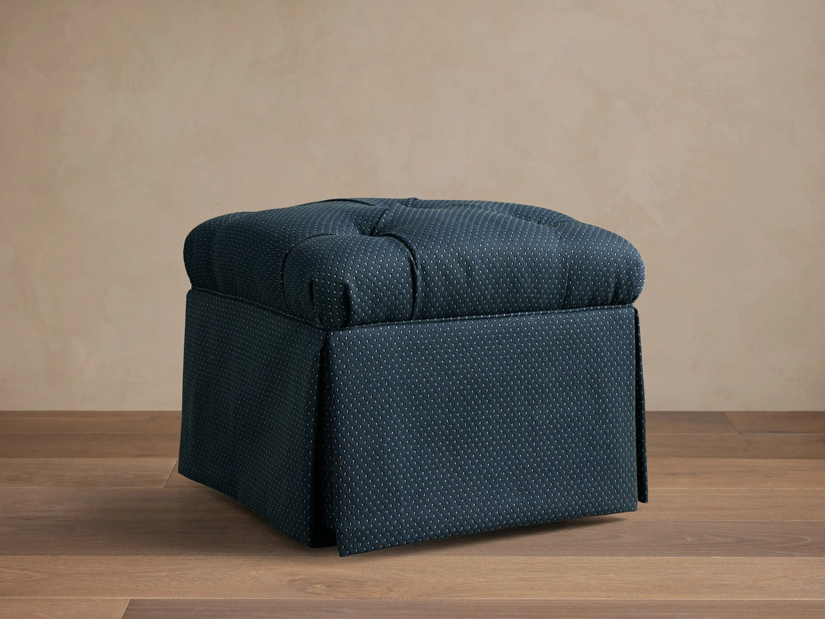 Front view of the dark blue dotted Liddie Square Ottoman with a tufted top and a skirted base.