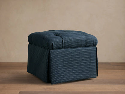 Front view of the dark blue dotted Liddie Square Ottoman with a tufted top and a skirted base.