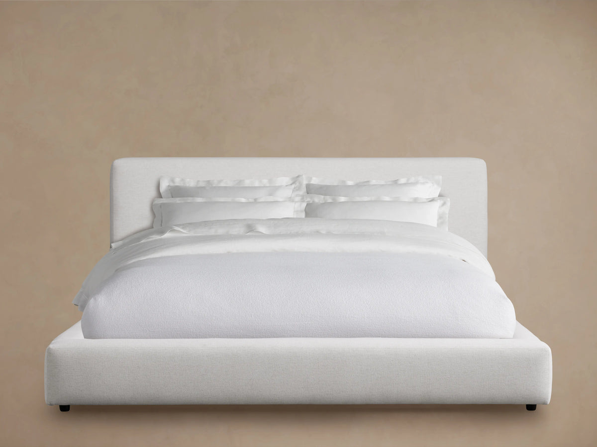 A white Lago Bed with a minimalist design, upholstered headboard, and bedding set on a neutral background.