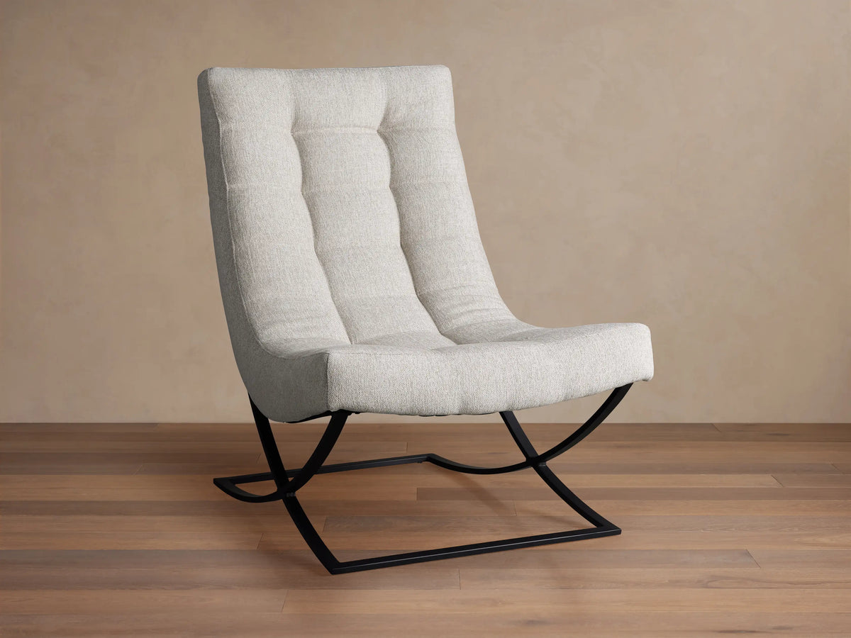Lloyd Chair: Modern light grey fabric chair with a tall, padded back and seat, on a unique black metal X-frame base, angled on wood floor.