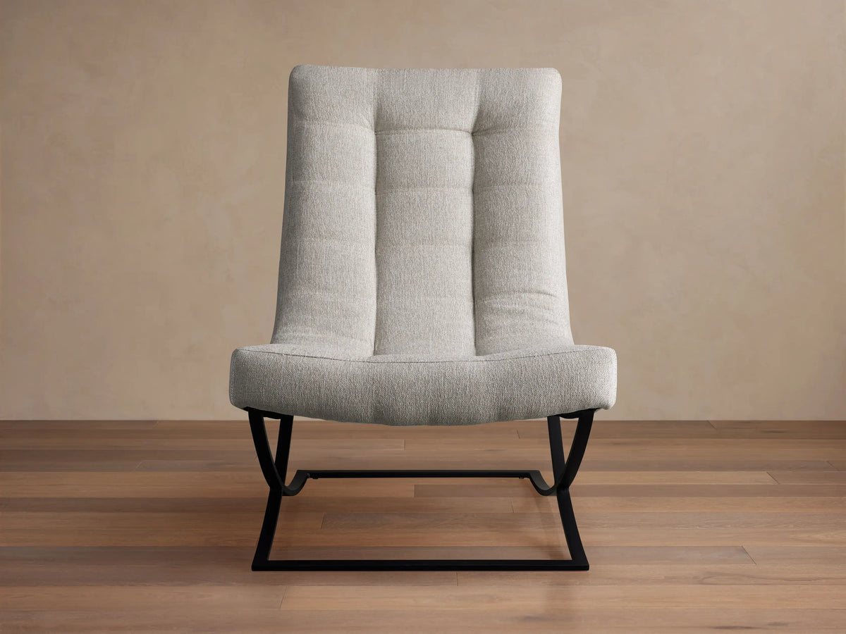 Lloyd Chair: Modern light grey fabric chair with a tall, padded back and seat, on a unique black metal X-frame base, angled on wood floor.