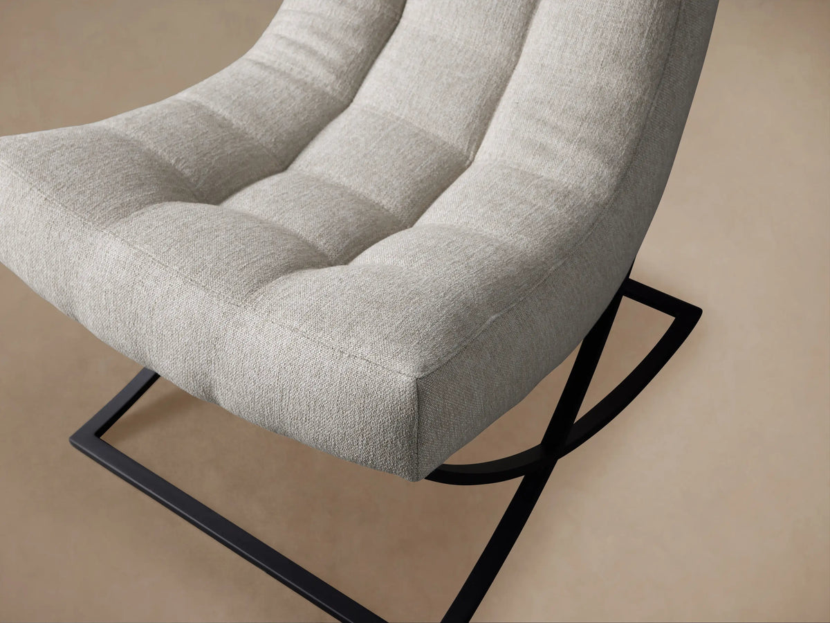 Lloyd Chair, front view. Light grey upholstered chair with a three-section tufted back and black angular metal base on a wooden floor.
