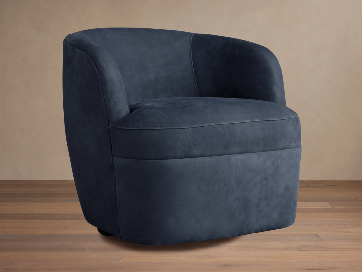 Dark blue nubuck leather swivel chair with rounded back and plush seat, angled slightly right on a wooden floor.