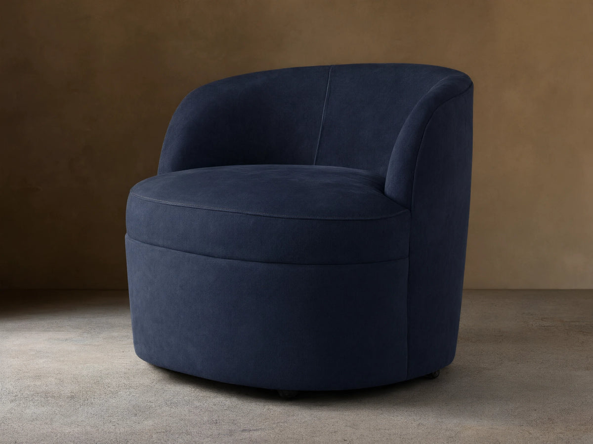 Dark blue nubuck leather swivel chair with rounded back and plush seat, angled slightly right on a wooden floor.