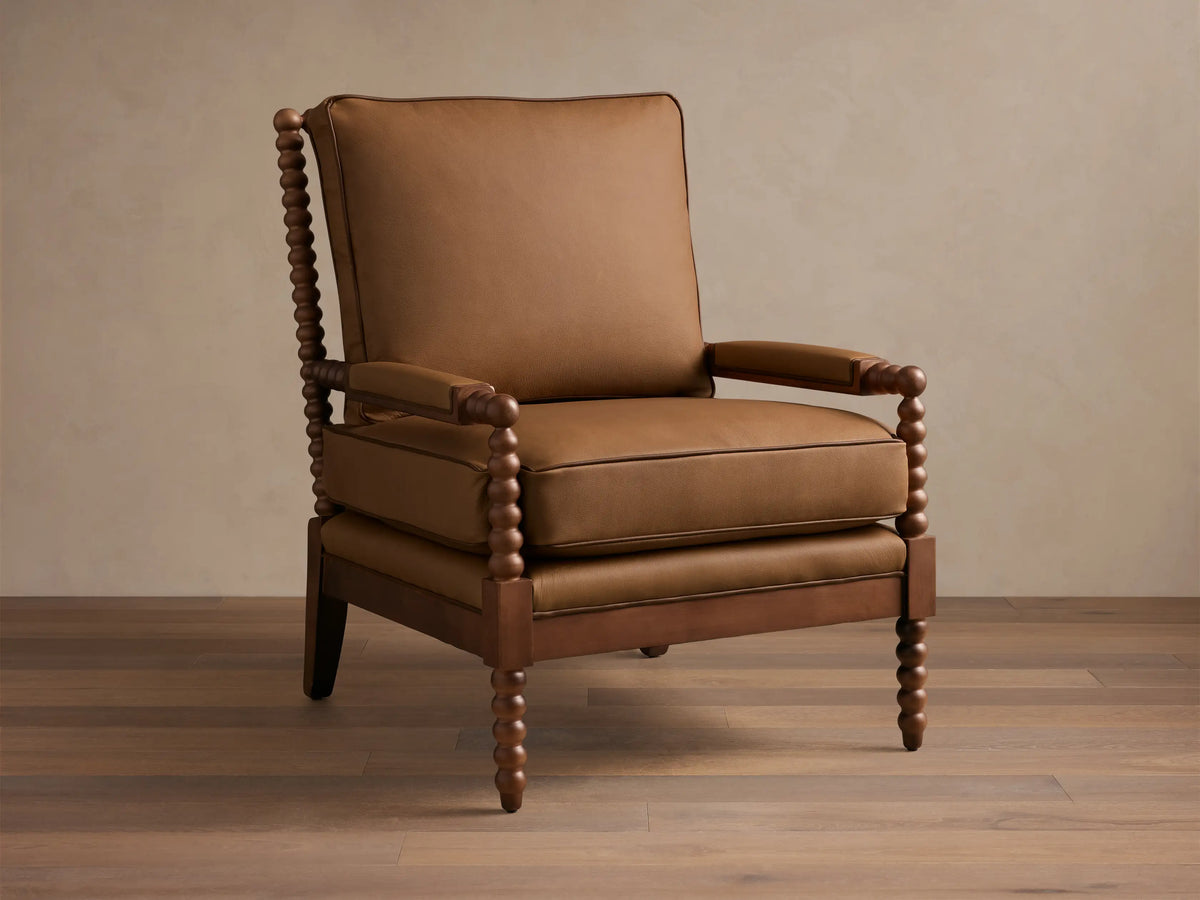 Front-quarter view of the brown Milly Leather Chair, showcasing its spindled dark wood arms and legs and plush upholstered cushions.