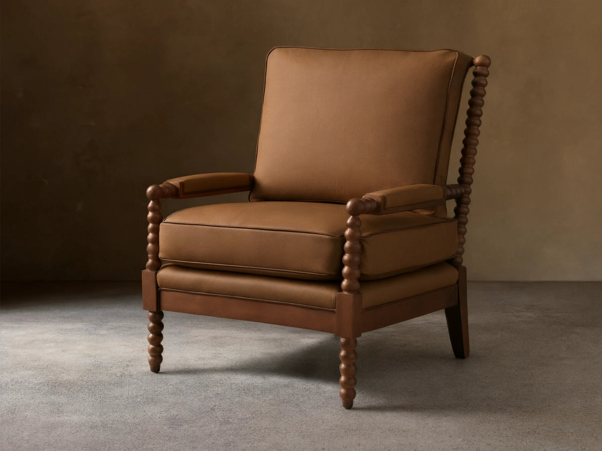 Front-quarter view of the brown Milly Leather Chair, showcasing its spindled dark wood arms and legs and plush upholstered cushions.