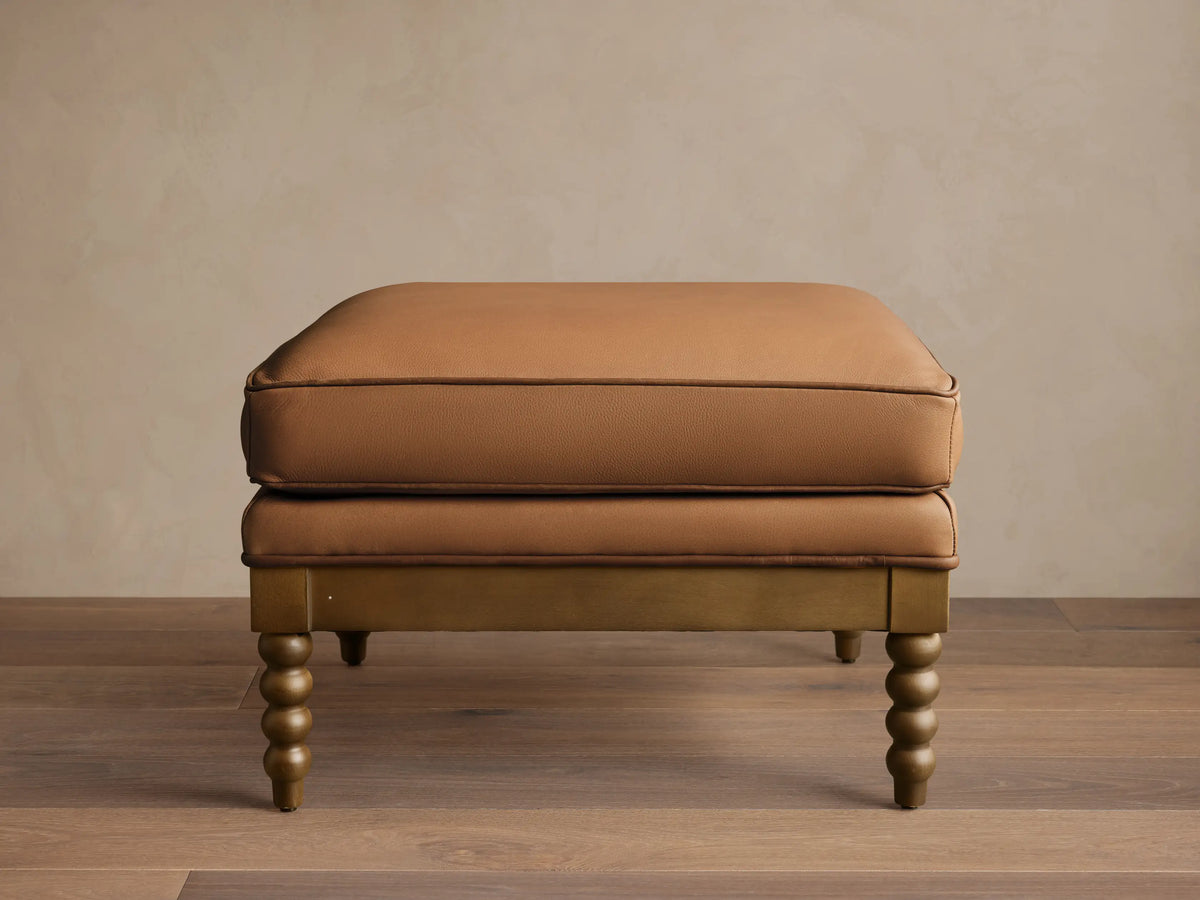Front view of the brown Milly Leather Ottoman with piped cushions and turned wood legs.