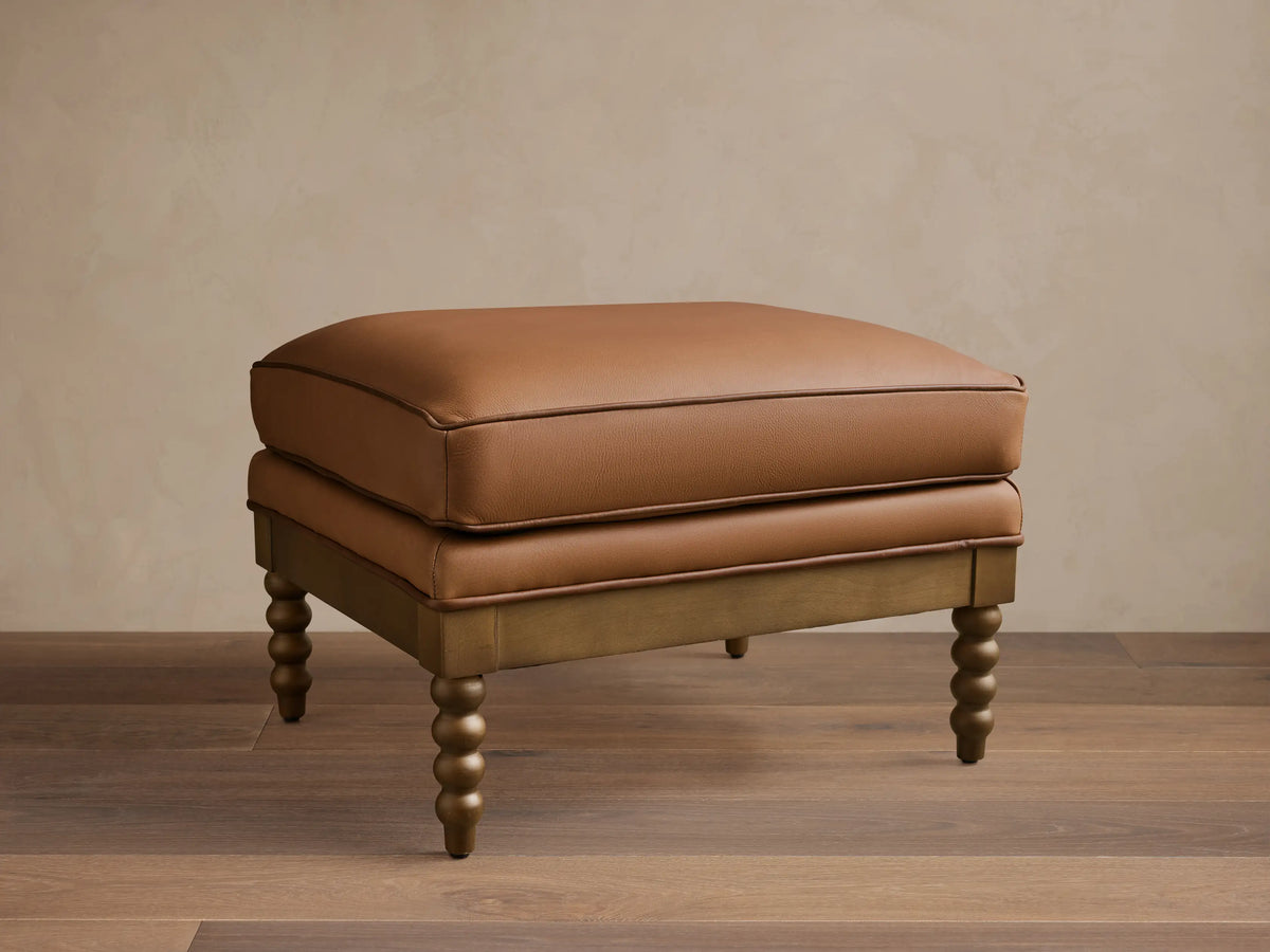 Front view of the brown Milly Leather Ottoman with piped cushions and turned wood legs.
