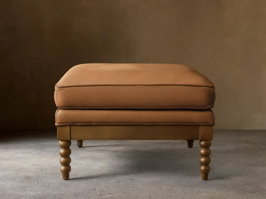 Front view of the brown Milly Leather Ottoman with piped cushions and turned wood legs.