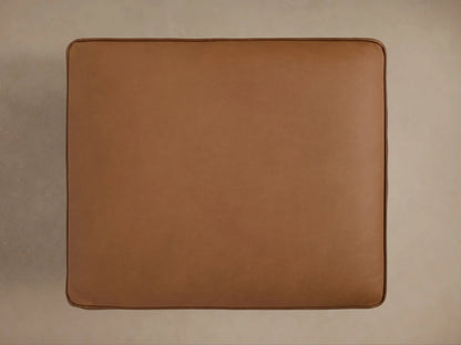 Angled view of a cognac leather Milly Leather Ottoman, featuring piped cushions, a natural wood frame, and turned legs.
