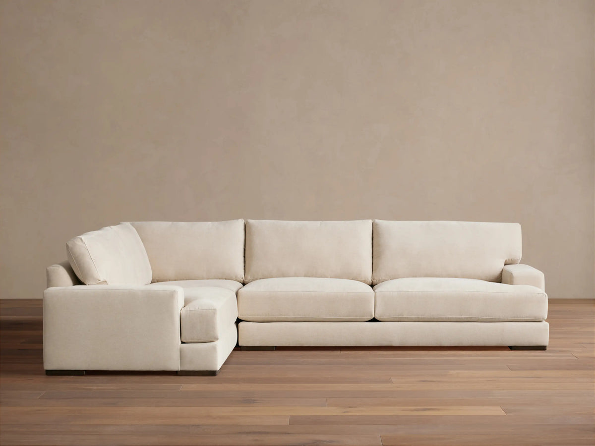 Beige Norwalk two-piece sectional on wooden floor, featuring plush cushions and L-shaped design against a neutral wall.