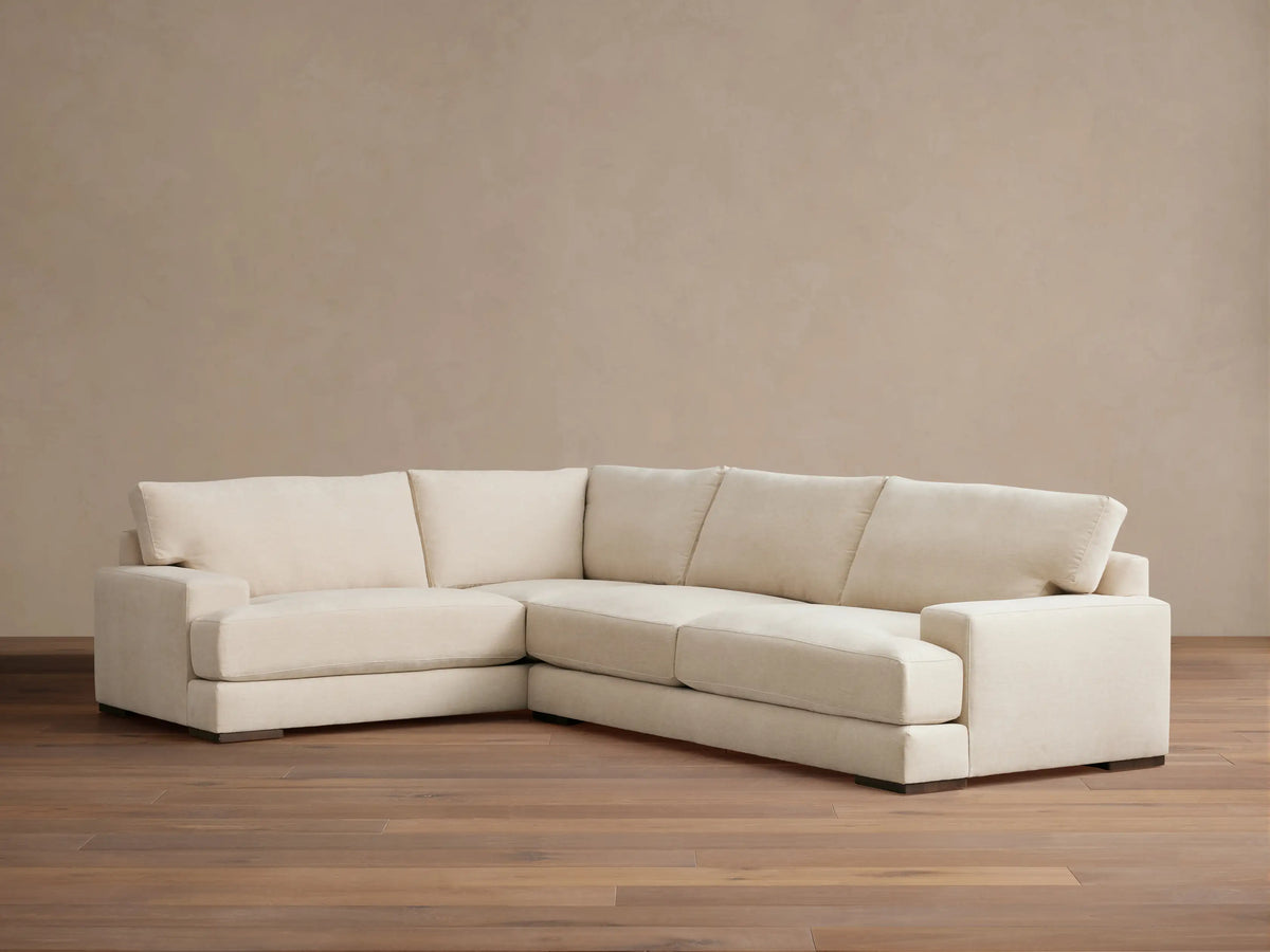 Beige Norwalk two-piece sectional on wooden floor, featuring plush cushions and L-shaped design against a neutral wall.