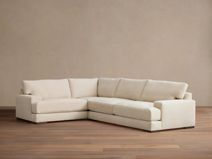 Beige Norwalk two-piece sectional on wooden floor, featuring plush cushions and L-shaped design against a neutral wall.