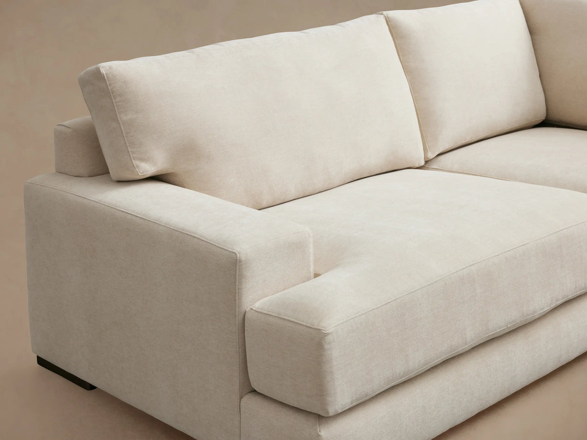 Norwalk Two-Piece Sectional in beige fabric, L-shaped design with plush seat and back cushions, on a wooden floor.