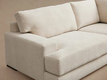 Norwalk Two-Piece Sectional in beige fabric, L-shaped design with plush seat and back cushions, on a wooden floor.