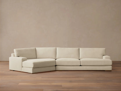 A beige Norwalk Two-Piece Cuddle Chaise Sectional on a wooden floor against a plain light-colored wall, featuring a chaise on the left.
