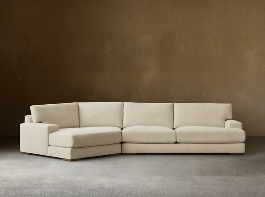 A beige Norwalk Two-Piece Cuddle Chaise Sectional on a wooden floor against a plain light-colored wall, featuring a chaise on the left.