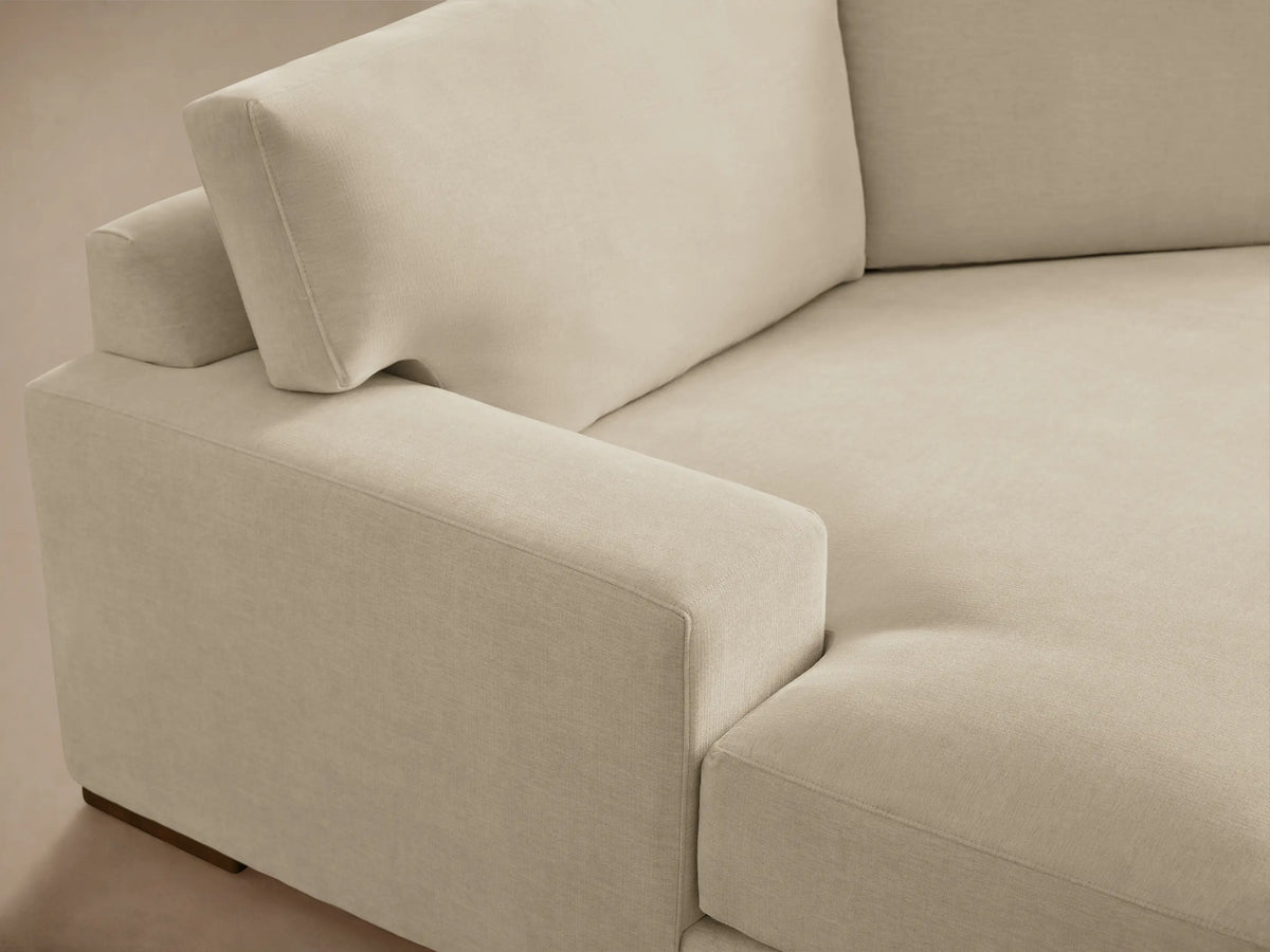 A beige Norwalk Two-Piece Cuddle Chaise Sectional with plush cushions, left-arm chaise, and right-arm sofa on a wooden floor.