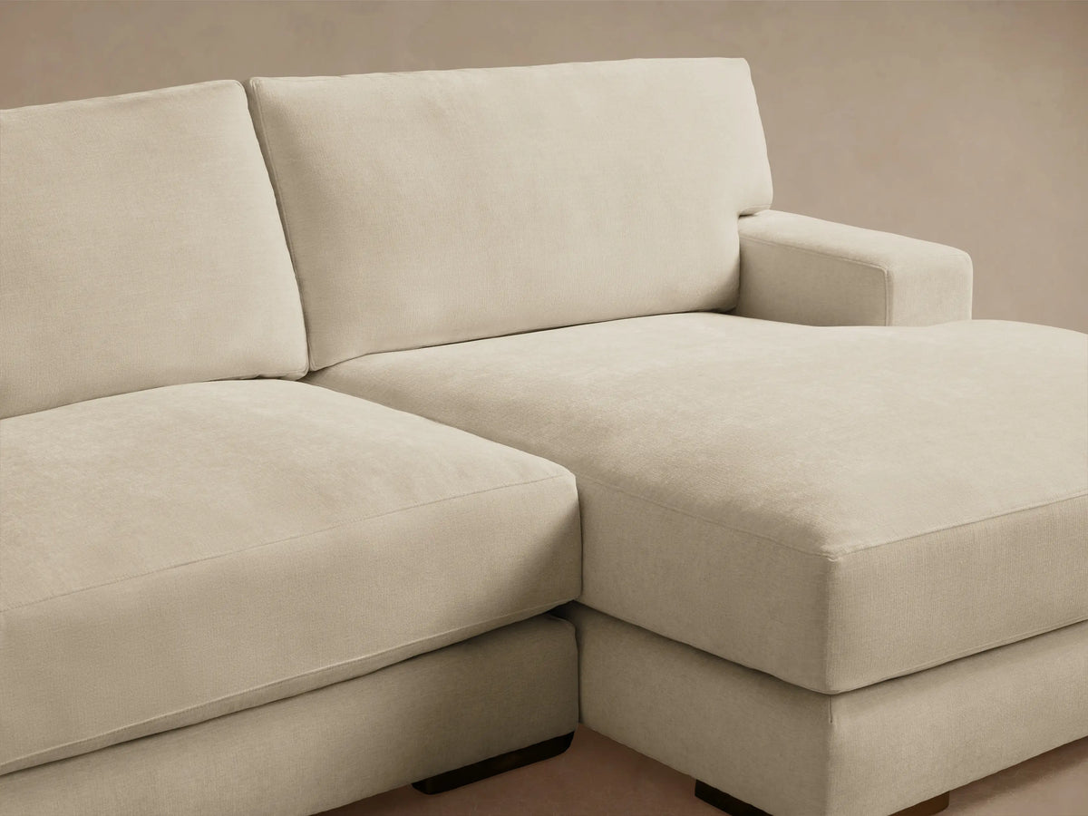 Norwalk Two-Piece Chaise Sectional in light beige fabric, featuring a left-arm sofa and right-arm chaise on wooden floor. Neutral wall backdrop.