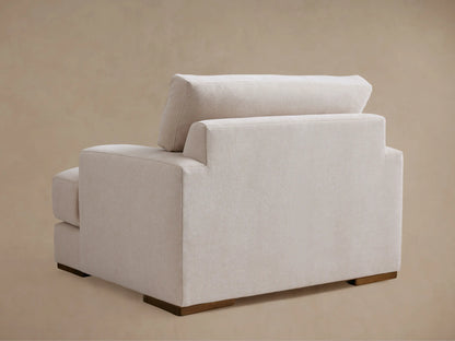 Norwalk Chair in side profile showing plush cushioned seat and backrest in light beige fabric, supported by dark wooden legs.