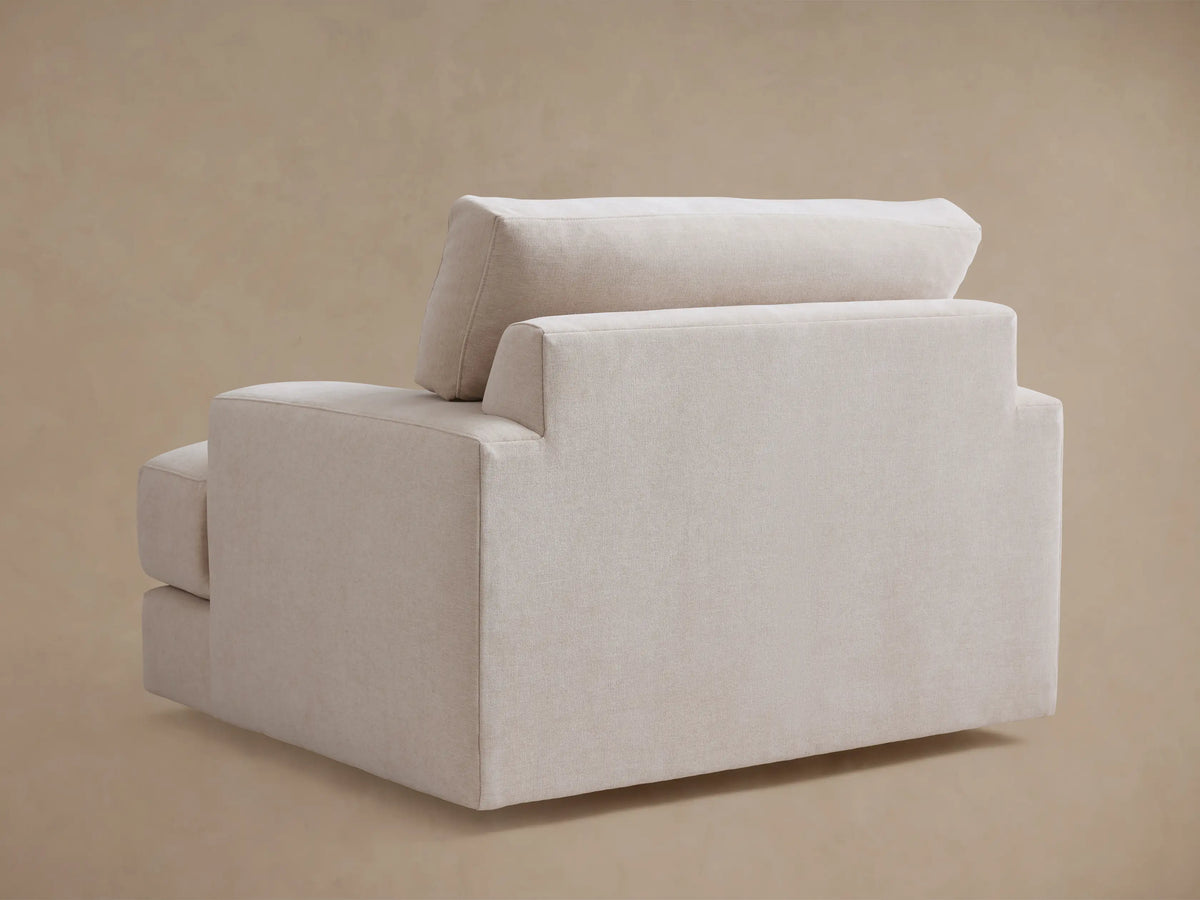 The Norwalk Swivel Chair shown from the side, featuring light beige upholstery, wide armrests, and plush cushions against a neutral background.