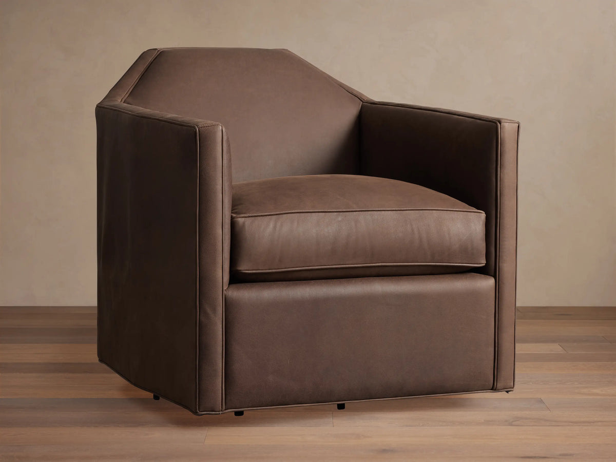 Marina Leather Swivel Chair. Brown leather armchair with an angular design, plush cushion, and integrated swivel base on wood floor.