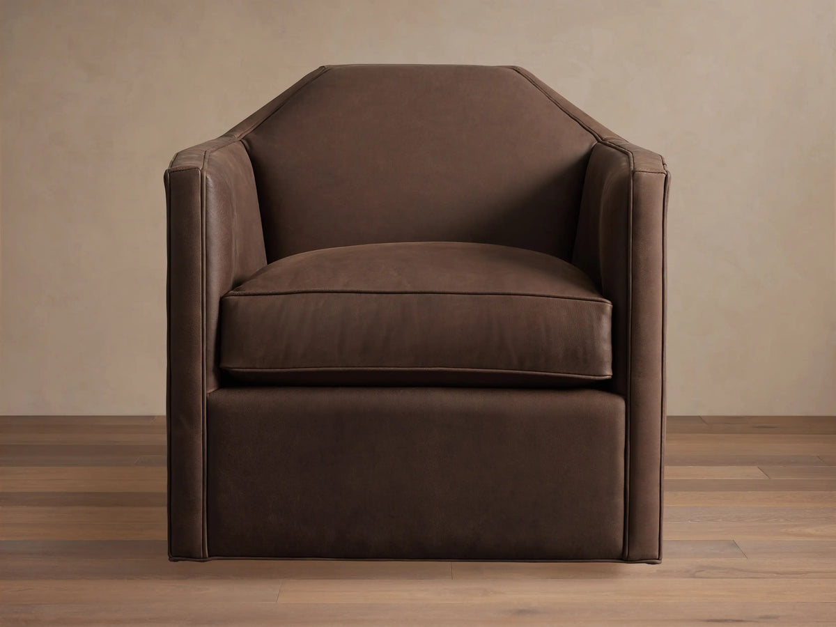 Marina Leather Swivel Chair. Brown leather armchair with an angular design, plush cushion, and integrated swivel base on wood floor.