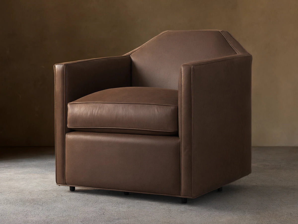 Marina Leather Swivel Chair. Brown leather armchair with an angular design, plush cushion, and integrated swivel base on wood floor.
