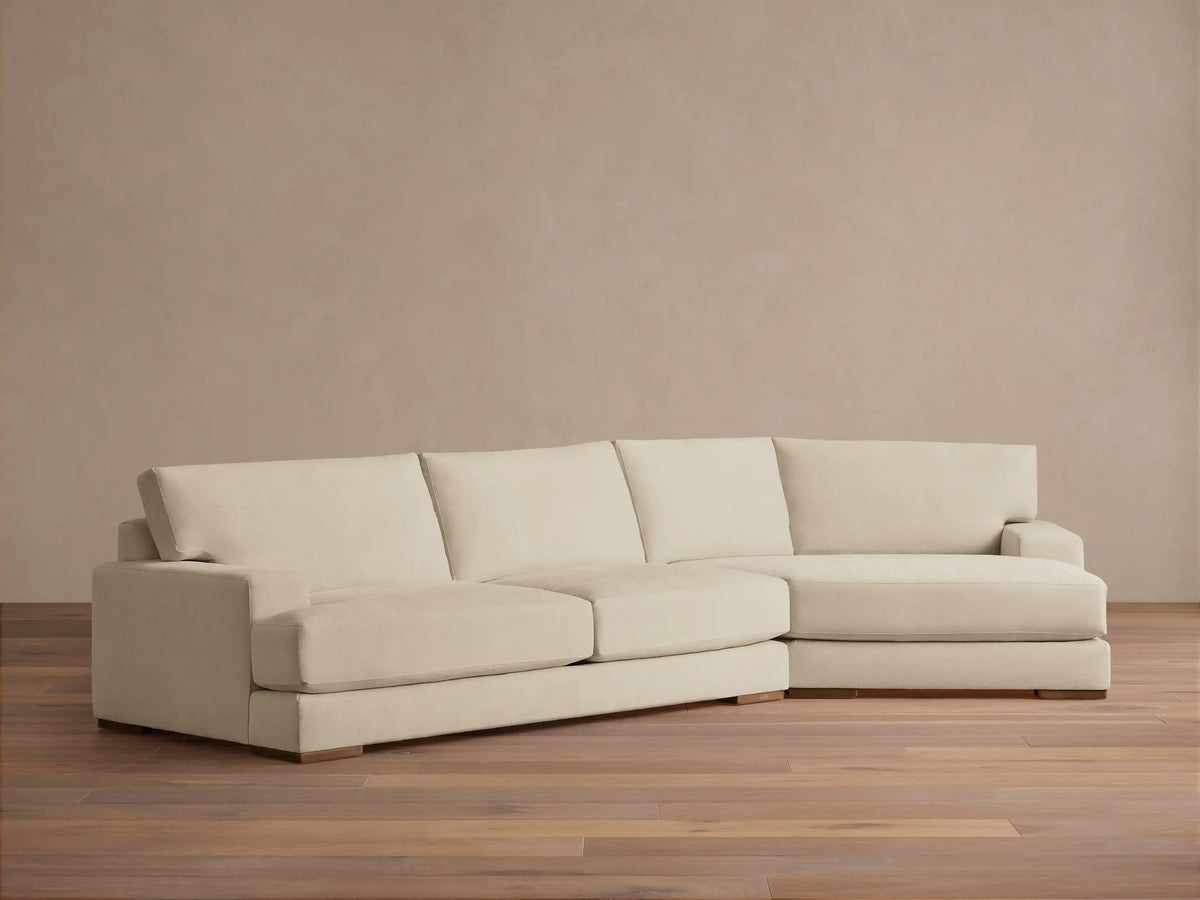 Norwalk Two-Piece Cuddle Chaise Sectional in light beige, L-shaped with three seat cushions and a chaise on the right. Set on wooden floor.