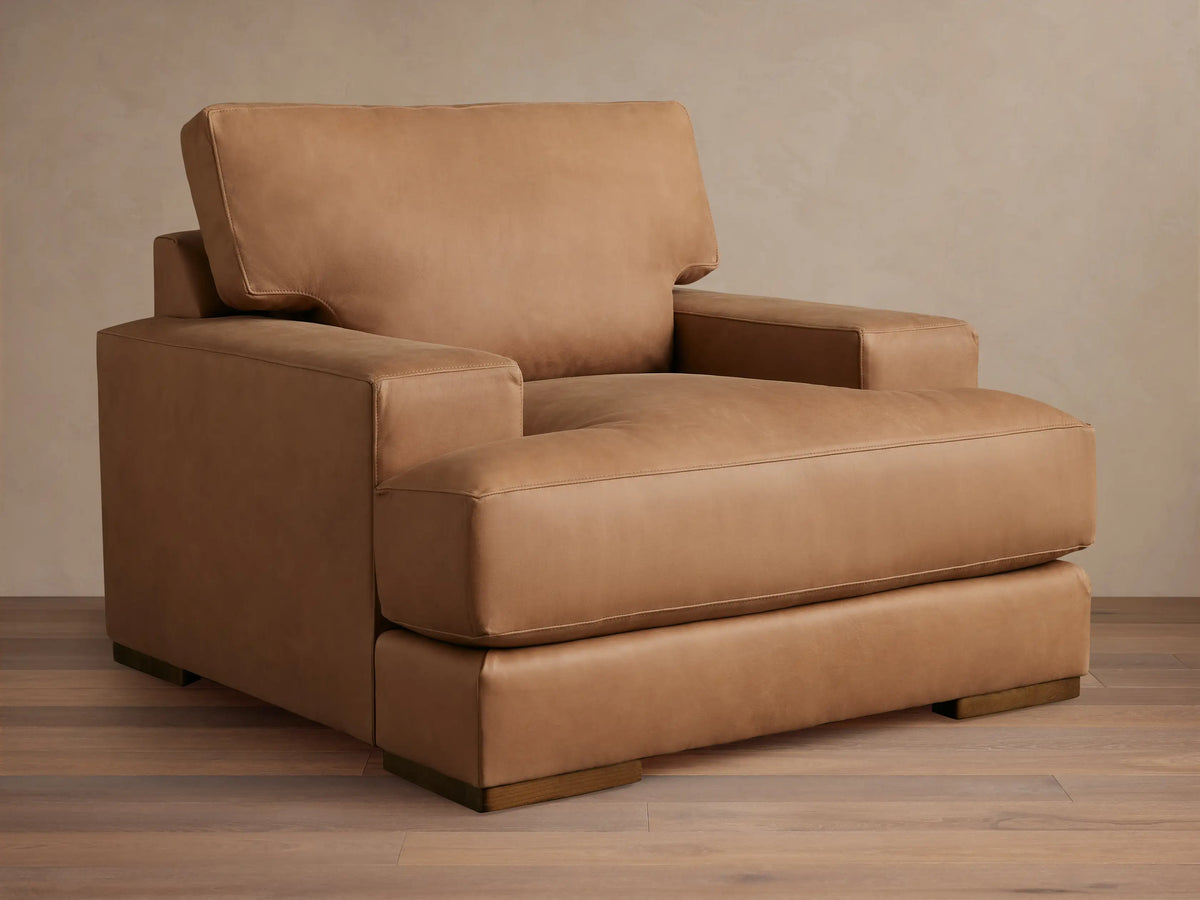Tan Norwalk Leather Chair with boxy design, wide armrests, plush seat, and back cushion. Positioned on wooden legs.