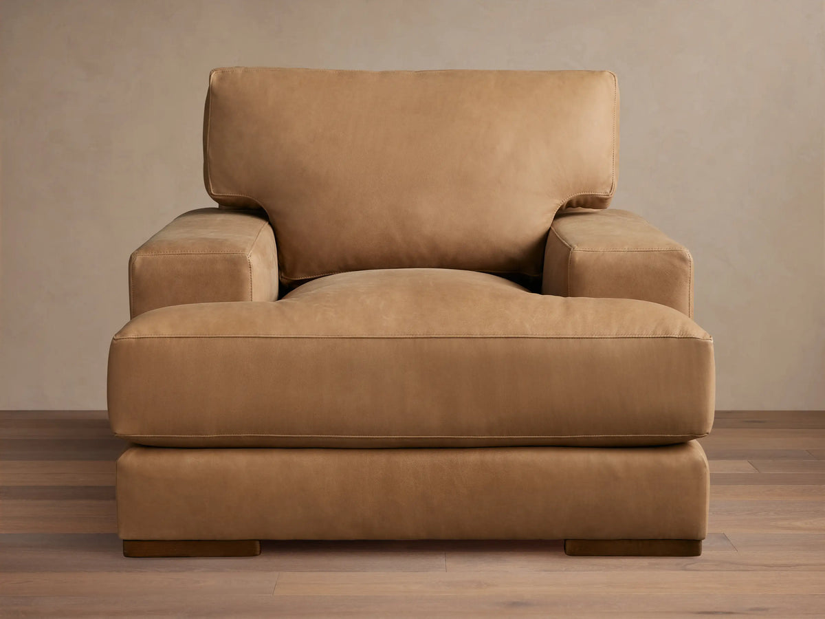 Tan Norwalk Leather Chair with boxy design, wide armrests, plush seat, and back cushion. Positioned on wooden legs.