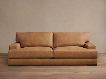 Tan leather Norwalk Sofa with two backrest cushions and sleek armrests placed on a wooden floor against a neutral wall.